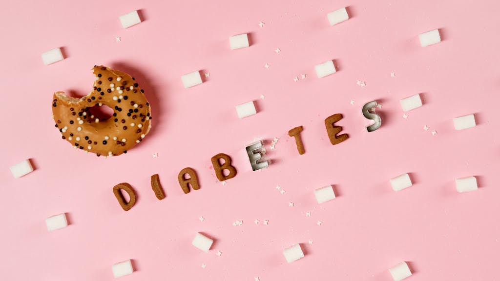 Creative depiction of diabetes with a donut, sugar cubes, and letters on a pink background.